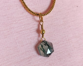May include: A gold chain necklace with a green and white agate pendant. The pendant is a hexagonal shape with a faceted design.