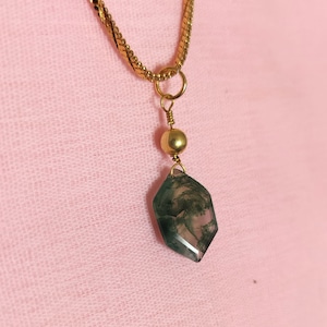 Può includere: Una collana con catena dorata con un ciondolo in agata verde e bianca. Il ciondolo ha una forma geometrica sfaccettata.