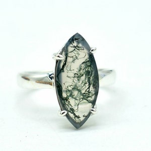 Peut inclure: Une bague en argent avec une pierre d'agate mousse de forme marquise. La pierre est de couleur vert clair et blanc avec un motif dendritique.