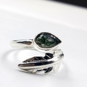 Könnte beinhalten: Ein silberner Ring mit einem grünen Moosachat-Stein und einem Federdesign. Der Ring ist verstellbar und kann an jedem Finger getragen werden.