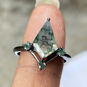 Könnte beinhalten: Ein silberner Ring mit einem großen, grünen Moosachat-Edelstein in geometrischer Form. Der Ring ist mit drei kleineren grünen Edelsteinen verziert.