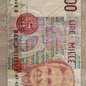 Può includere: Una banconota italiana da 1000 lire. La banconota presenta il testo "BANCA D'ITALIA" e "1000 LIRE MILLE". La banconota ha un ritratto e un design complesso con vari colori.