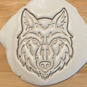 Puede incluir: Un cortador de galletas de plástico blanco en forma de cabeza de lobo. La cabeza de lobo está detallada con un patrón de pelaje texturizado y tiene una expresión feroz.