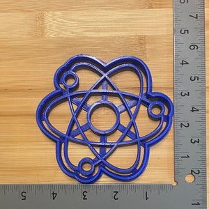 May include: A blue plastic cookie cutter shaped like an atom. The cutter is about 2 inches in diameter.