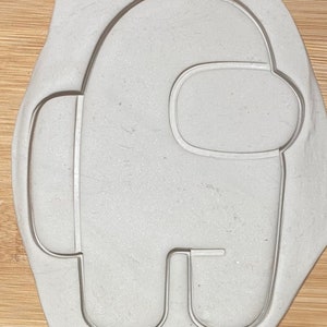 Può includere: Un tagliapasta in plastica bianca a forma di personaggio di Among Us. Il tagliapasta ha un corpo arrotondato con una piccola visiera e una sola gamba.