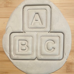 May include: A white clay mold with three square impressions. The impressions are shaped like alphabet blocks with the letters A, B, and C.