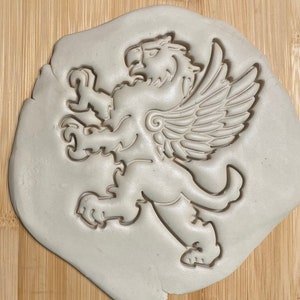 May include: A white plastic cookie cutter in the shape of a griffin, a mythical creature with the head and wings of an eagle and the body of a lion.