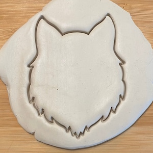 Puede incluir: Un cortador de galletas de plástico blanco en forma de cabeza de lobo. El cortador está sobre una superficie blanca.