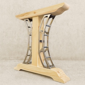 May include: A wooden table base with a light-colored finish. The base features a rectangular top and bottom with curved edges. Two metal supports with an arched design connect the top and bottom.