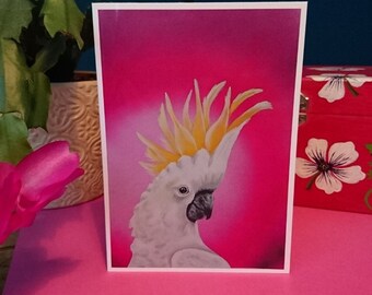 以下が含まれることがあります： ピンクの背景に、黄色い冠羽を持つ白いコカトゥーが描かれています。鳥は右を向いており、黒い目を持っています。