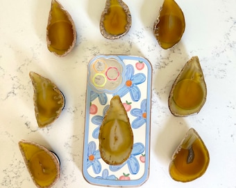 May include: A phone case with a blue and white floral design and a clear agate phone ring holder. The phone case is surrounded by eight agate slices in a teardrop shape.