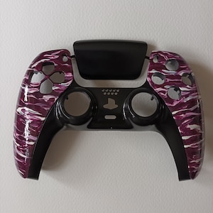 May include: A black and purple PlayStation 5 controller with a camouflage pattern. The controller is missing the face buttons and the analog sticks.