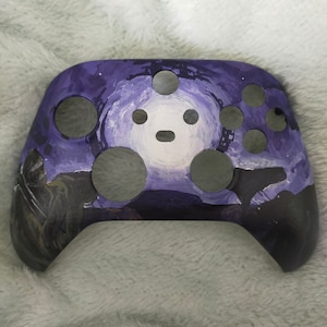 May include: A purple and black Xbox controller with a custom painted design featuring a starry night sky with a white moon and a silhouette of a person.