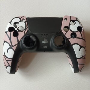 以下が含まれることがあります： 白と黒の雲のデザインが施された、黒とピンクのPlayStation 5コントローラーです。