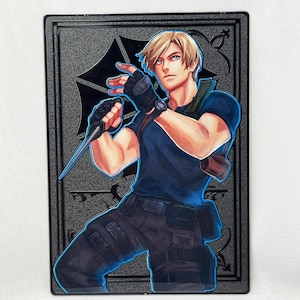 May include: A black and silver metal pin featuring a character from a video game. The character is a man with blond hair, wearing a blue shirt, black pants, and a black holster. He is holding a knife in his right hand and has a serious expression on his face.