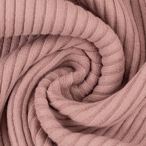 May include: Close-up of a soft, pink ribbed fabric. The fabric is folded and twisted, creating a swirling pattern.
