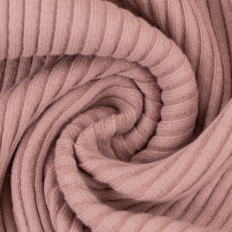 May include: Close-up of a soft, pink ribbed fabric. The fabric is folded and twisted, creating a swirling pattern.
