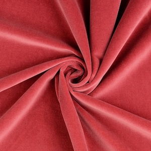 Puede incluir: Primer plano de una tela de terciopelo suave de color rosa con una textura lisa. La tela está doblada y drapeada, creando un patrón de remolino.