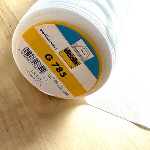 Könnte beinhalten: Eine weiße Rolle Wieseline G 785 Stoff, 100% PES, 90 cm x 25 m. Das Etikett ist gelb mit schwarzem Text und einem weißen Logo.