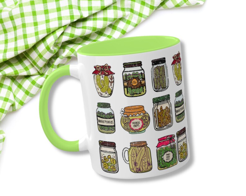 K&ouml;nnte beinhalten: Eine wei&szlig;e Keramiktasse mit gr&uuml;nem Rand zeigt eine farbenfrohe Illustration verschiedener Gl&auml;ser, gef&uuml;llt mit Gurken, Gurkenchips und s&uuml;&szlig;en Gurken. Die Tasse ist perfekt f&uuml;r Gurkenliebhaber.