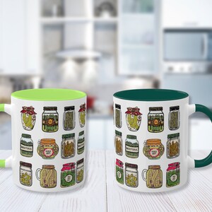 K&ouml;nnte beinhalten: Zwei Keramik-Kaffeebecher mit wei&szlig;em Hintergrund und einem Muster aus Gl&auml;sern, die mit Gurken gef&uuml;llt sind. Ein Becher hat einen gr&uuml;nen Rand und der andere einen dunkelgr&uuml;nen Rand.