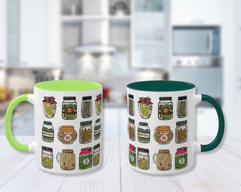 K&ouml;nnte beinhalten: Zwei Keramik-Kaffeebecher mit wei&szlig;em Hintergrund und einem Muster aus Gl&auml;sern, die mit Gurken gef&uuml;llt sind. Ein Becher hat einen gr&uuml;nen Rand und der andere einen dunkelgr&uuml;nen Rand.