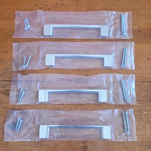 May include: Four sets of silver-colored cabinet pulls, each packaged in a clear plastic bag. Each set includes a rectangular handle and screws for installation. The handles are a simple, modern design.