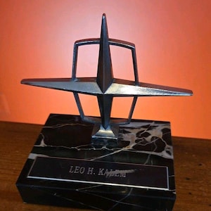 Può includere: Scultura in metallo argentato con design a stella, montata su una base in marmo nero con venature bianche. La base presenta una placca rettangolare con l'iscrizione "LEO H. KALEM". La scultura ha un'estetica moderna della metà del secolo. La base è lunga circa 15 cm.