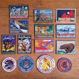 May include: A collection of embroidered patches featuring national parks and scouting themes. Patches include images of Yosemite, Grand Canyon, and Bryce Canyon, along with scouting emblems. The patches are rectangular and circular, with various colors and designs.