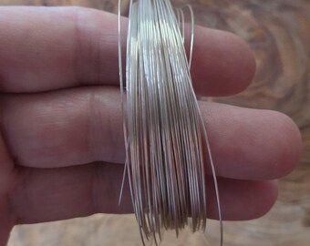 May include: A bundle of thin, silver-colored wire held in a hand. The wire appears to be tightly wound together, with individual strands visible. The background is a blurred wooden surface.
