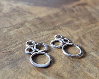 May include: Two pairs of silver earrings, each with a cluster of small, connected rings. Each earring features a larger, oval ring at the base. The earrings are presented on a wooden surface.
