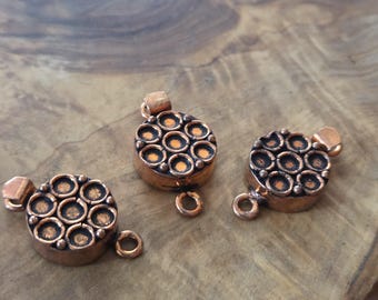 May include: Three copper-colored round clasps with a textured design of small circles. Each clasp has a small loop and a rectangular piece for attachment. The clasps are displayed on a wooden surface.