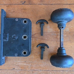 May include: A vintage black door lock set, comprising a rectangular lock plate, two skeleton keys, and a round doorknob with a long stem. The set is made of metal and appears to be antique.