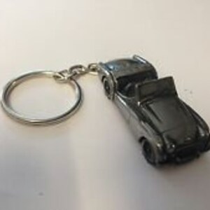 May include: A silver-colored metal keychain featuring a detailed model of a classic convertible car.
