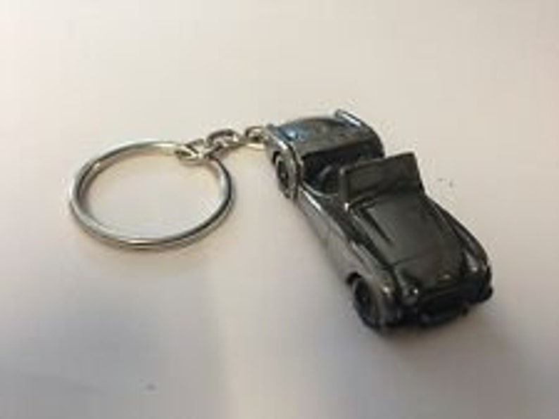 May include: A silver-colored metal keychain featuring a detailed model of a classic convertible car.