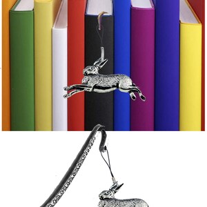 Puede incluir: Un marcapáginas de plata con un diseño detallado y un colgante de liebre de plata. El marcapáginas es curvo y tiene un borde decorativo. La liebre está en posición de salto.