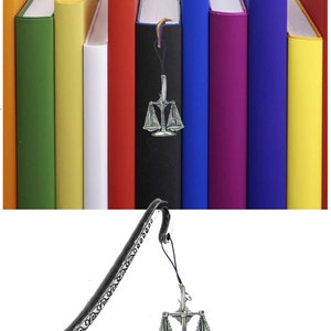 Könnte beinhalten: Ein silbernes Lesezeichen mit einem dekorativen Design und einem Anhänger einer Justitia-Waage. Das Lesezeichen hängt an einer Reihe bunter Bücher.