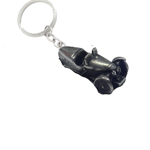 May include: A silver-colored metal keychain featuring a detailed miniature model of a vintage race car.