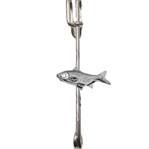 May include: Silver-toned fish-shaped brooch with a safety pin closure. The fish is detailed with scales and fins.