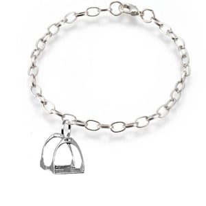 May include: A silver-colored bracelet with an oval link chain and a stirrup charm. The stirrup charm is a miniature replica of a horse riding stirrup. The bracelet is displayed on a white background.