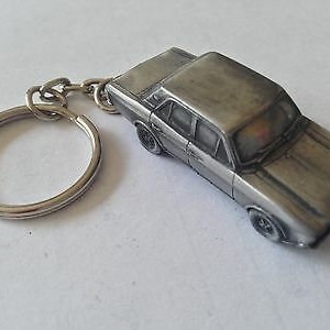 Puede incluir: Un llavero de metal plateado con un modelo detallado de un coche antiguo. El coche tiene un estilo de carrocería redondeado y un diseño clásico.