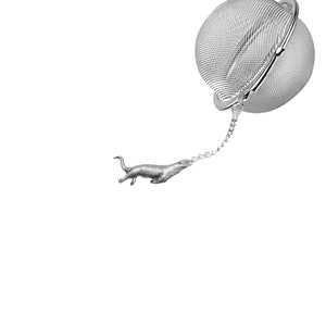 Puede incluir: Un infusor de té de plata con una cadena y una pequeña figura de nutria unida al extremo de la cadena.