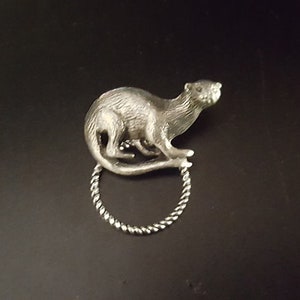 May include: A silver charm in the shape of an otter, with a twisted silver ring attached.