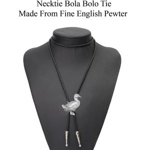 Pode incluir: Um bolo tie de pato prateado com cordão de couro preto. A gravata é exibida em um manequim de busto preto. O texto "Check out my range of Necklace Necktie Bola Bolo Tie Made From Fine English Pewter" está acima da imagem.