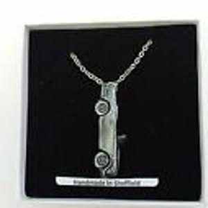 May include: A silver necklace with a pendant shaped like a car. The pendant is detailed with wheels and a windshield. The necklace is in a black box with a white label that says "Handmade in Sheffield".