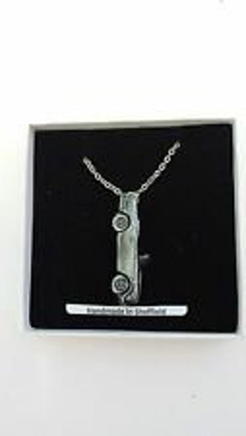 May include: A silver necklace with a pendant shaped like a car. The pendant is detailed with wheels and a windshield. The necklace is in a black box with a white label that says "Handmade in Sheffield".