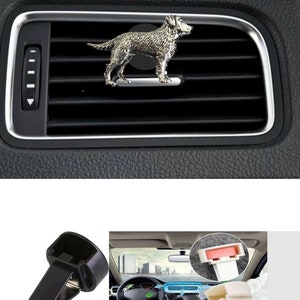 May include: Two black car vent clips for hanging air fresheners. The clips are made of plastic and have a spring-loaded mechanism to hold the air freshener in place. The clips are shown in a car interior with a dog-shaped air freshener.