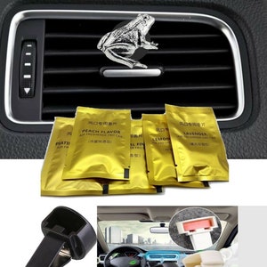 May include: A set of four car air fresheners in gold foil pouches with different scents: Peach, Lemon, Lavender, and Floral. The pouches are labeled in Chinese and English. Two black plastic car vent clips are shown, one with a frog figurine on top.