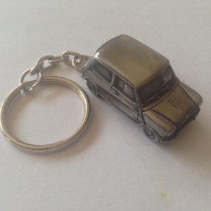 Peut inclure: Un porte-clés en métal argenté représentant une miniature d'une voiture Mini Cooper classique.