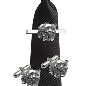 May include: A black tie with a silver tie clip and cufflinks featuring a bear design.